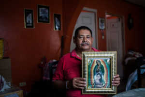Jesús René Maradiaga, un líder de la comunidad, sostiene una imagen de la Virgen de Guadalupe con un retrato de su hija, Yury Tatiana Maradiaga, que fue asesinada en 2005. Credit Katie Orlinsky para The New York Times